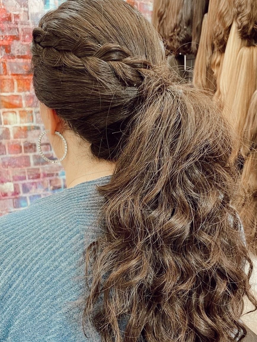 A braided ponytail with loose curls, styled in front of the wig wall at the Miri salon.