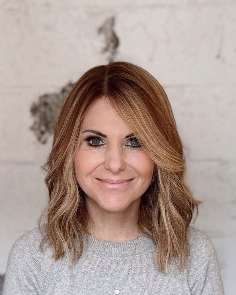 Shoulder-length wavy lob in light brown with blonde highlights, worn with a pale pink top.