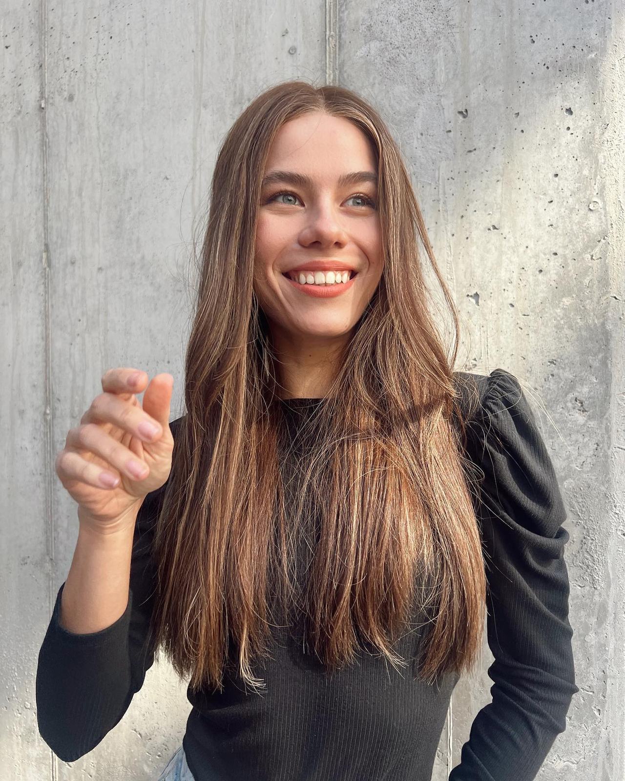 Long, sleek straight dark brown hair with soft highlights, against a raw concrete wall.