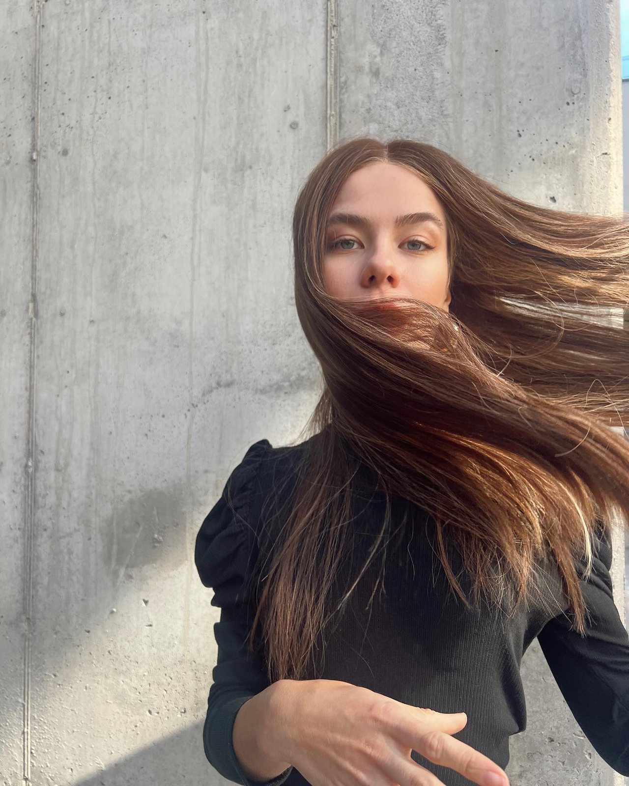 Windswept straight dark hair in an editorial portrait against a pale wall.